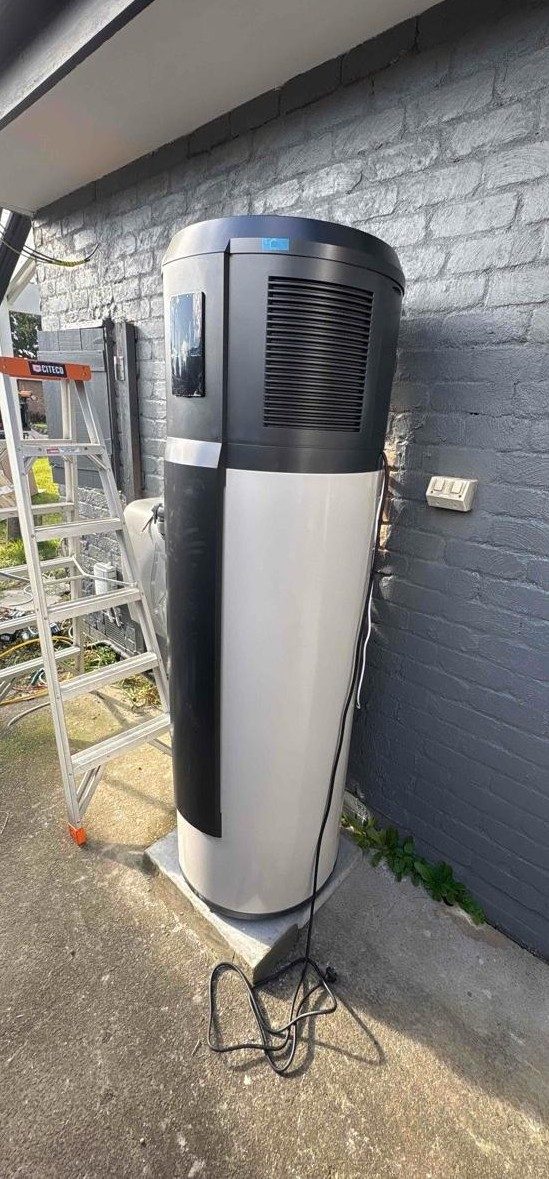 Haier heat-pump hot water unit installed against the exterior brick wall of daniel's baxter home