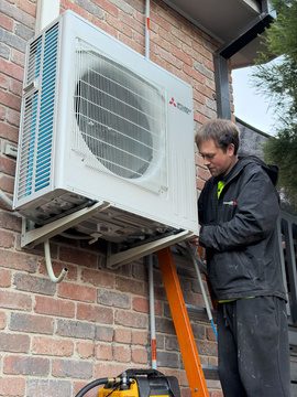 Installer fitting the outdoor mitsubishi electric compressor unit to the brick wall