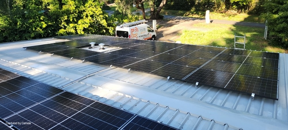 Aiko solar panels along a tin roof in emerald with a powerband electrical van parked below
