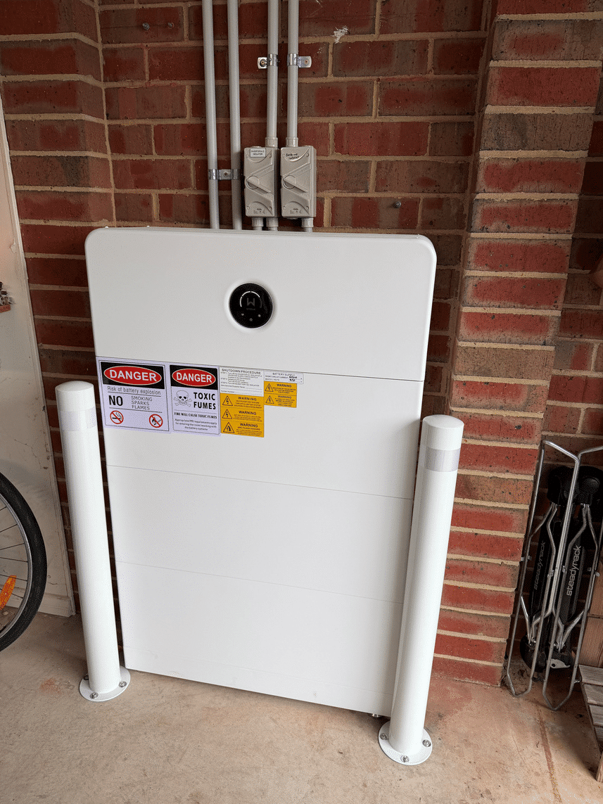 Home battery protected by bollards against a brick garage wall in safety beach