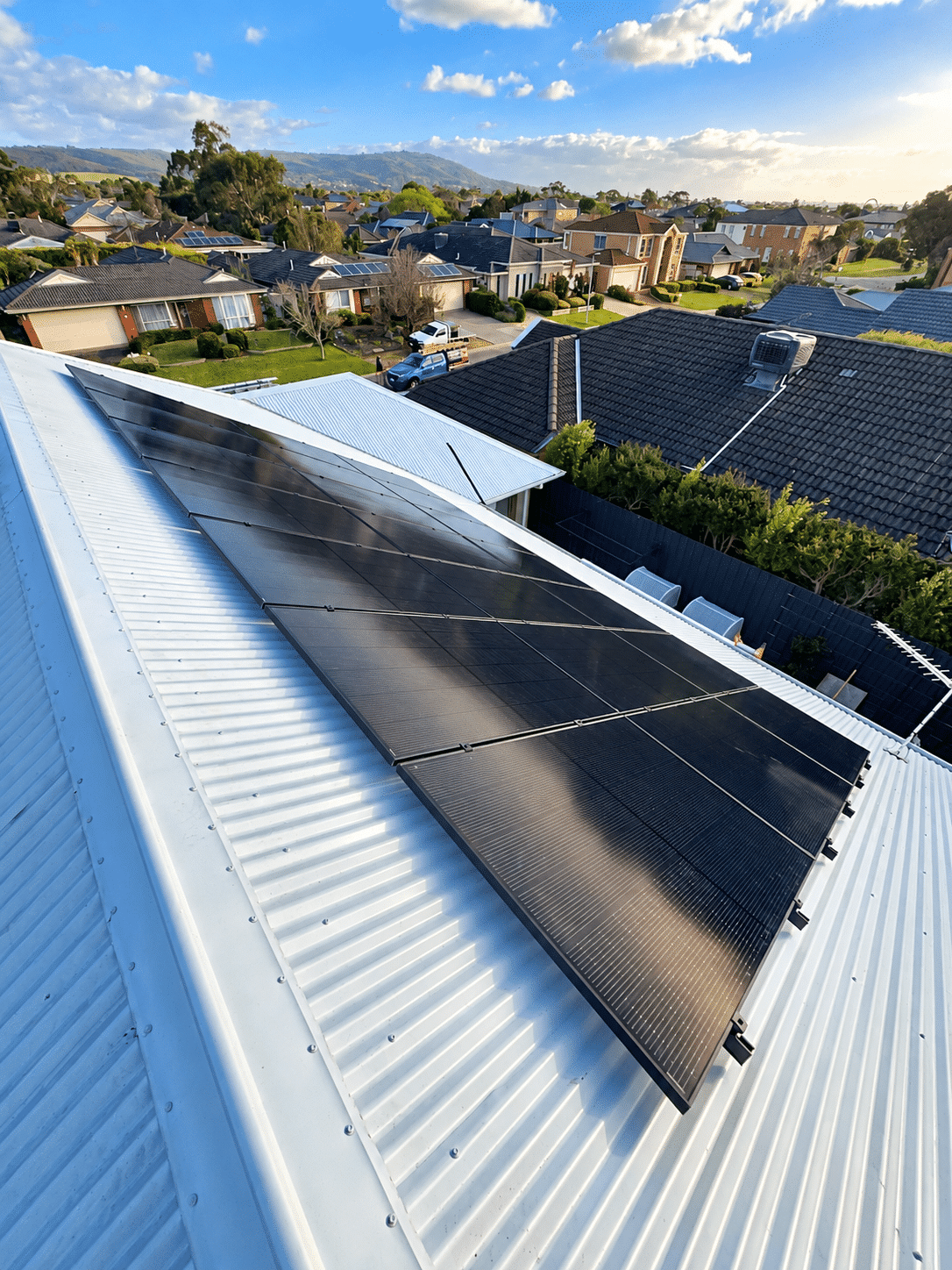 Aerial view of a large solar array on a safety beach home with neighbouring rooftops behind