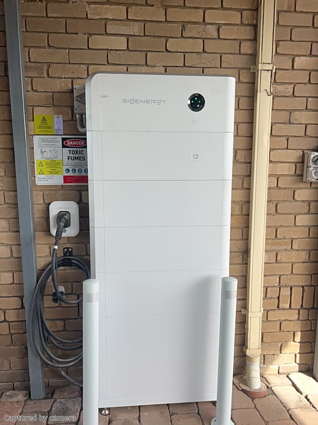 Sigenergy battery with bollards and an ev charger on the brick wall of a somerville home